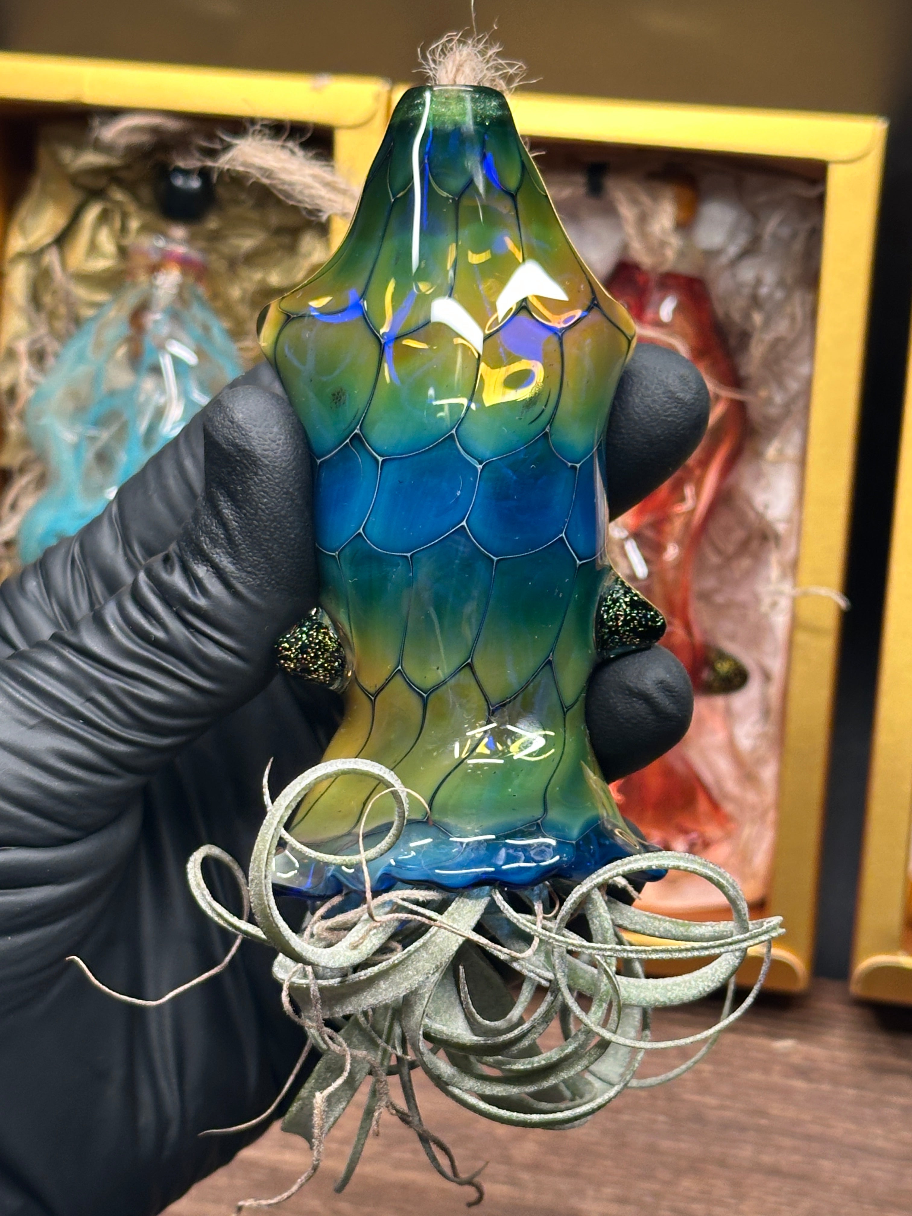 A flameworked and hand-spun blown glass squid air plant holder featuring detailed glass fins, custom eyes, and an integrated patented clip holding a live air plant.