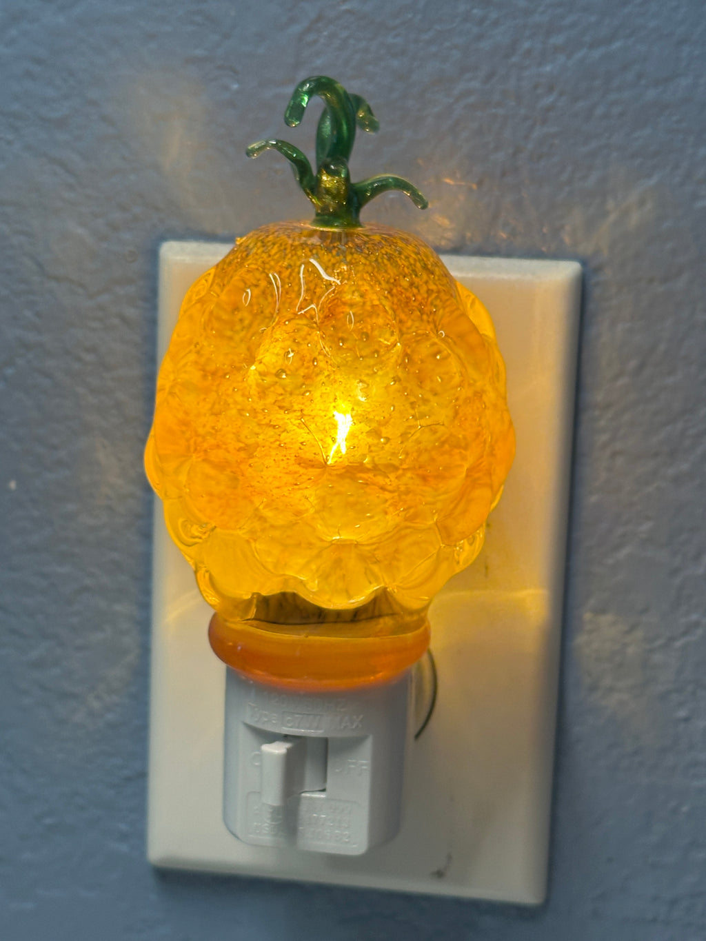 A flameworked and hand-spun blown glass pineapple night light featuring a detailed green crown and a textured yellow frit body that diffuses a warm, amber glow.