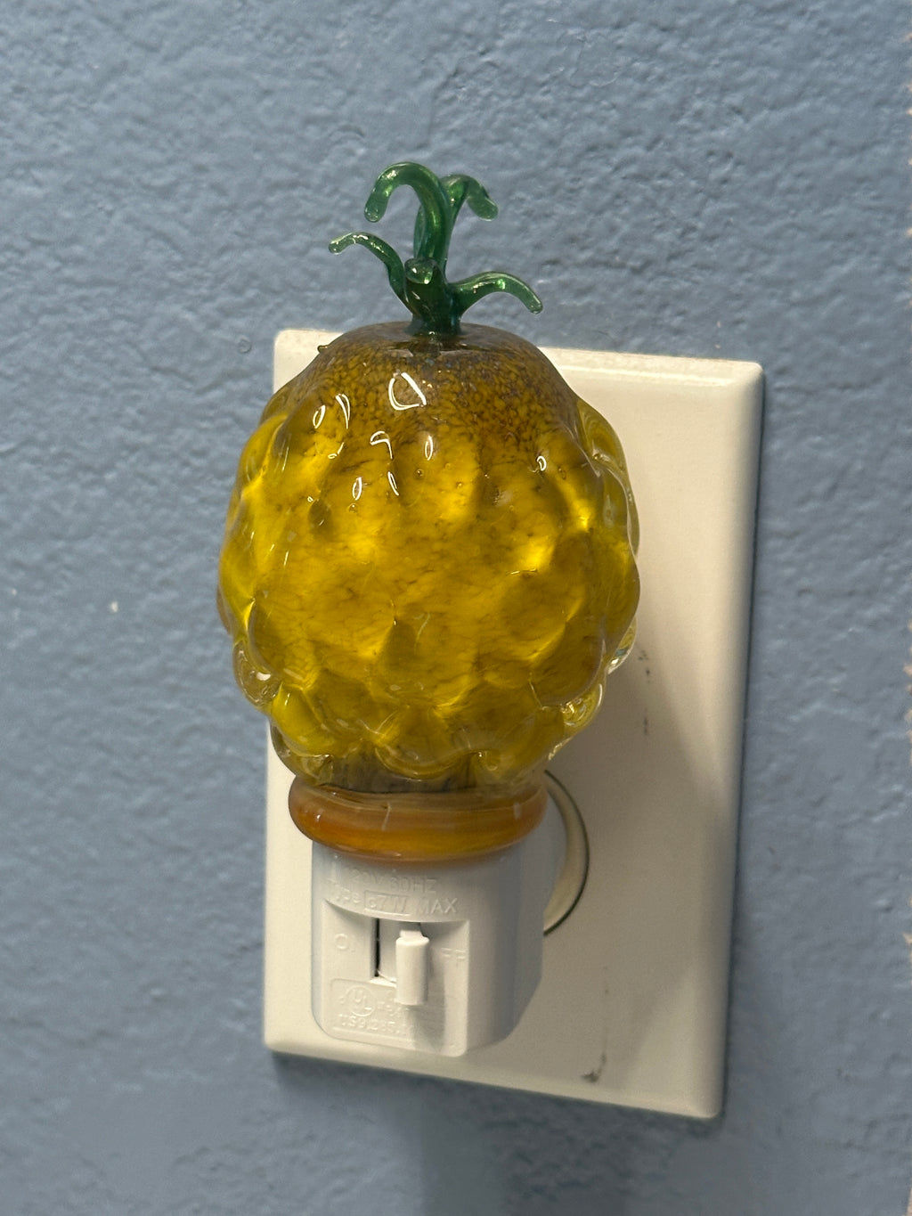 A flameworked and hand-spun blown glass pineapple night light featuring a detailed green crown and a textured yellow frit body that diffuses a warm, amber glow.