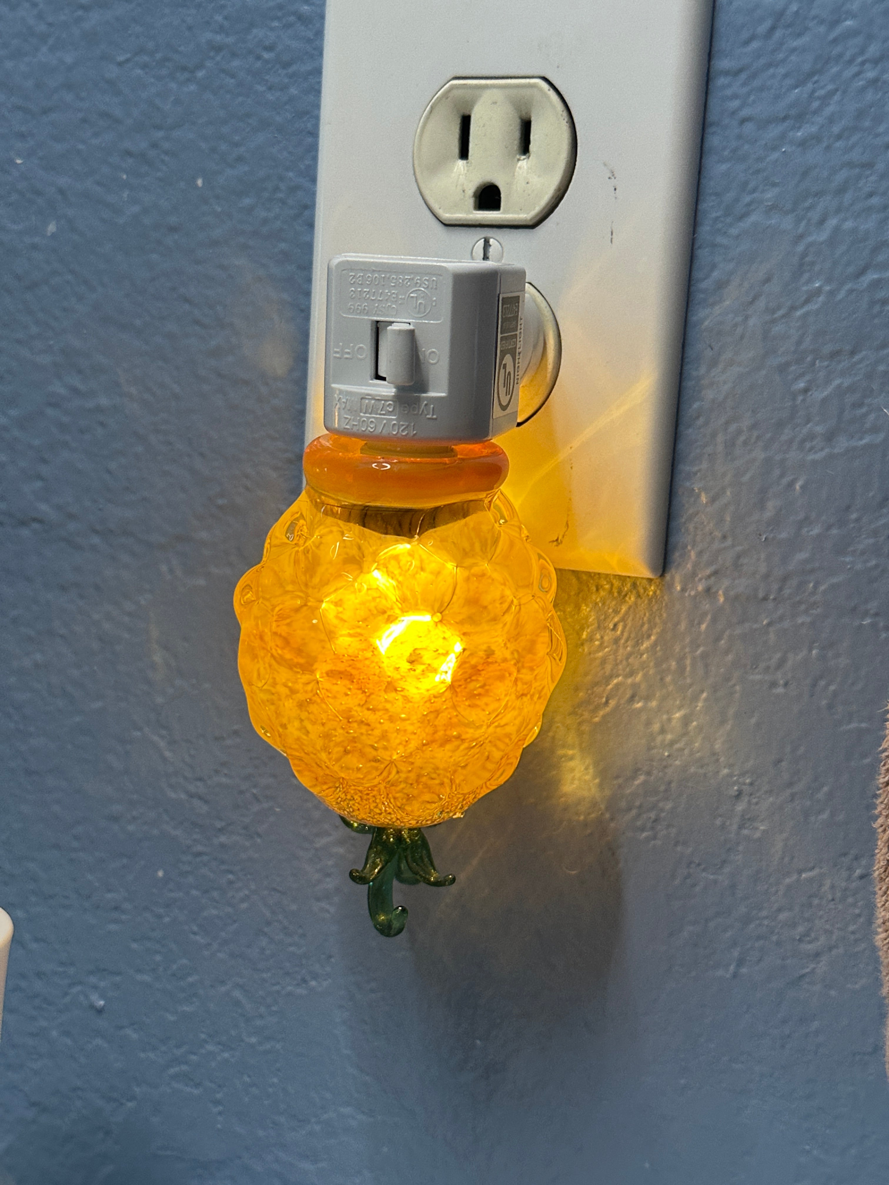 A flameworked and hand-spun blown glass pineapple night light featuring a detailed green crown and a textured yellow frit body that diffuses a warm, amber glow.