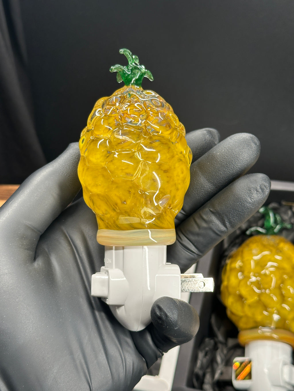 A flameworked and hand-spun blown glass pineapple night light featuring a detailed green crown and a textured yellow frit body that diffuses a warm, amber glow.